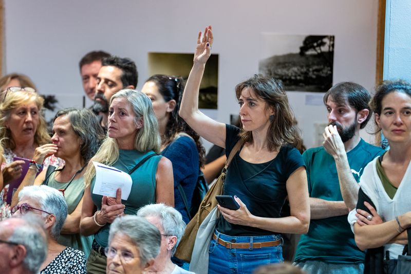 Una mujer levanta la mano para intervenir en una asamblea ciudadana, ejemplo de cómo la co-creación urbana fortalece el capital social y las redes vecinales.