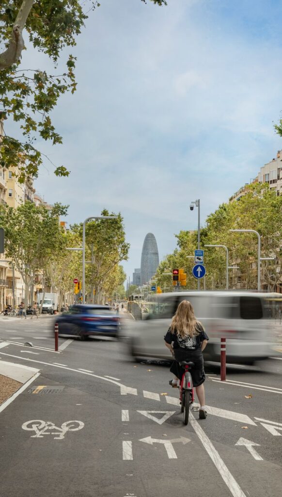 Ciclista esperando en un paso de peatones de un carril bici urbano con semáforo y vista de fondo hacia la Torre Glòries en Barcelona. Cyclist waiting at an urban bike lane crossing with traffic light and the Glòries Tower in the background in Barcelona.