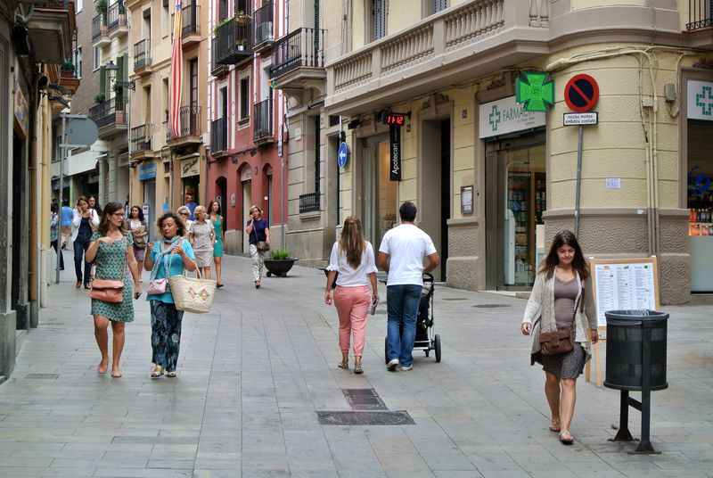 Peatones paseando por una calle pacificada con comercio local, reflejo del resultado de una estrategia de comunicación urbana exitosa. Pedestrians walking through a pedestrianized street with local shops, reflecting the outcome of a successful urban communication strategy.